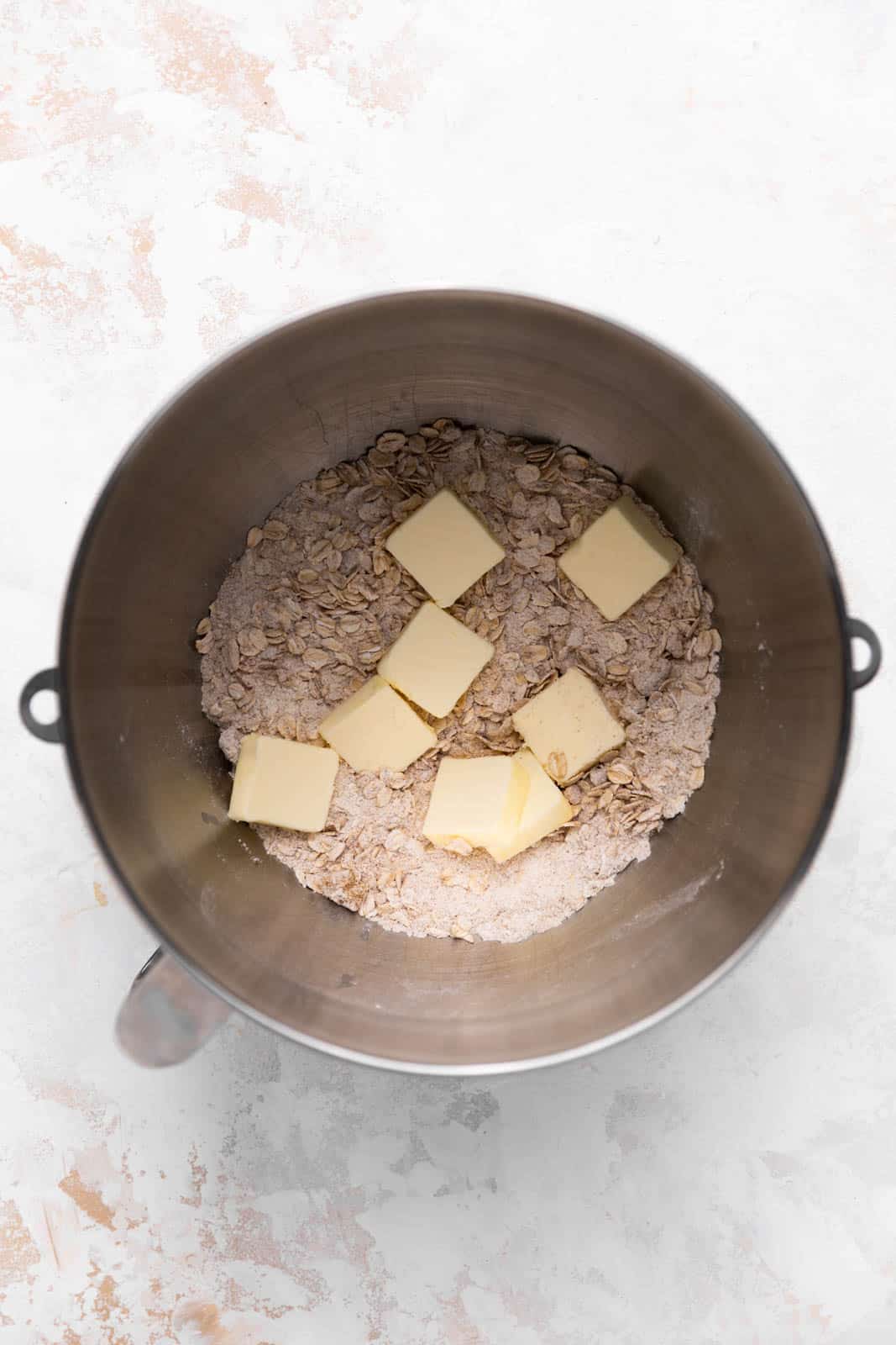 Tablespoons of butter on dry ingredients for crisp topping in a metal stand mixer mixing bowl set on a flat surface.