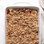 Unbaked crisp topping over a unbaked strawberry apple crisp in a white rectangular ceramic dish.
