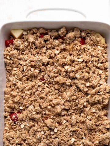 Unbaked crisp topping over a unbaked strawberry apple crisp in a white rectangular ceramic dish.