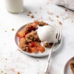 Baked strawberry apple crisp in a white round plate with a fork and scoop of vanilla ice cream with a glass of milk.