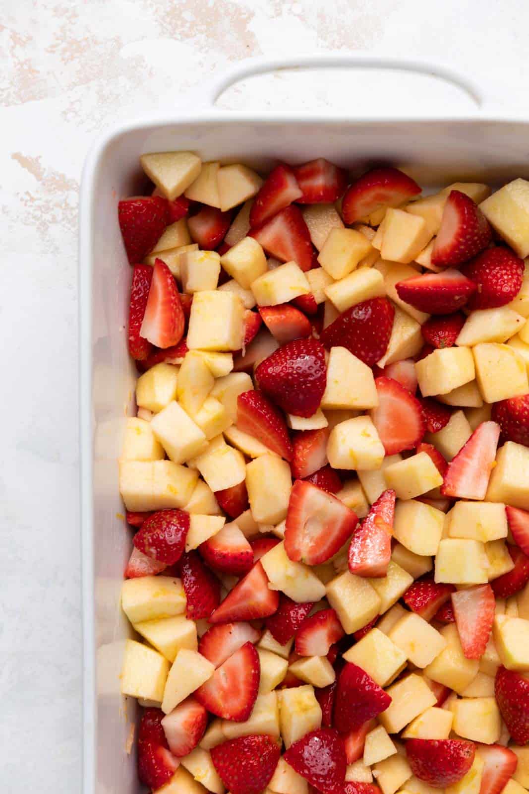 Unbaked strawberry and apple crisp filling spread in a white ceramic baking dish.