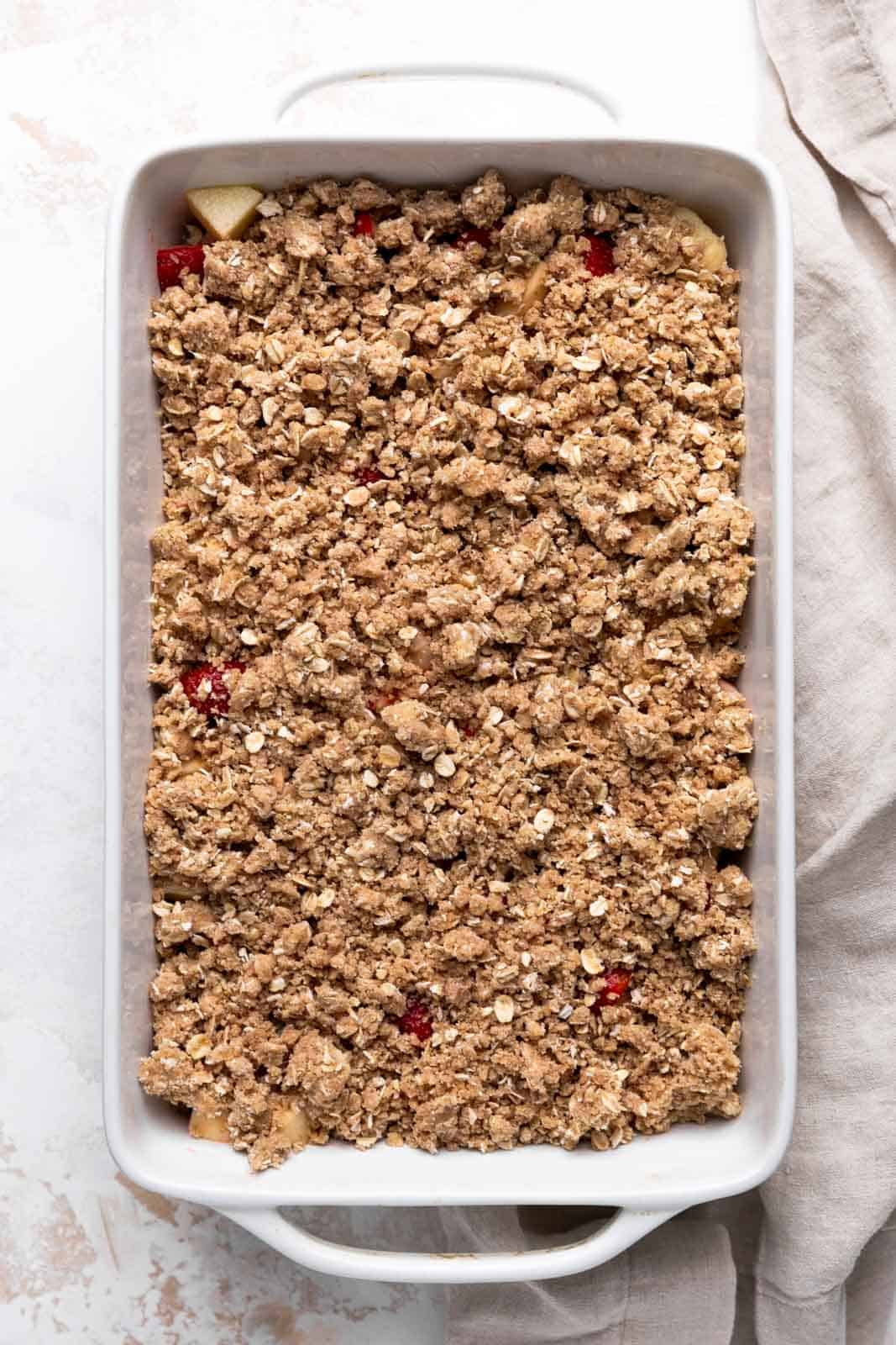 Unbaked strawberry apple crisp in a white rectangular ceramic baking dish set on a flat surface.