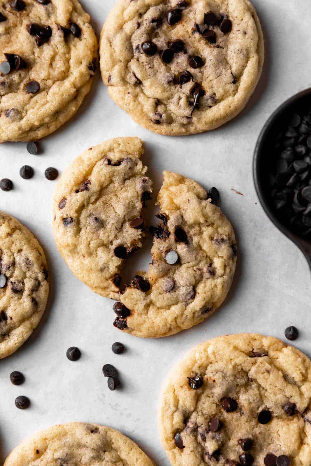 Overhead shot of chocolate chip sugar sugar cookies with mini chocolate chips arranged on a white parchment paper with one broken in half.