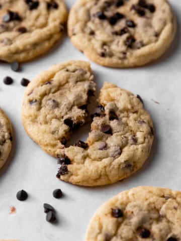Chocolate chip sugar sugar cookies with mini chocolate chips arranged on a white parchment paper with one broken in half.