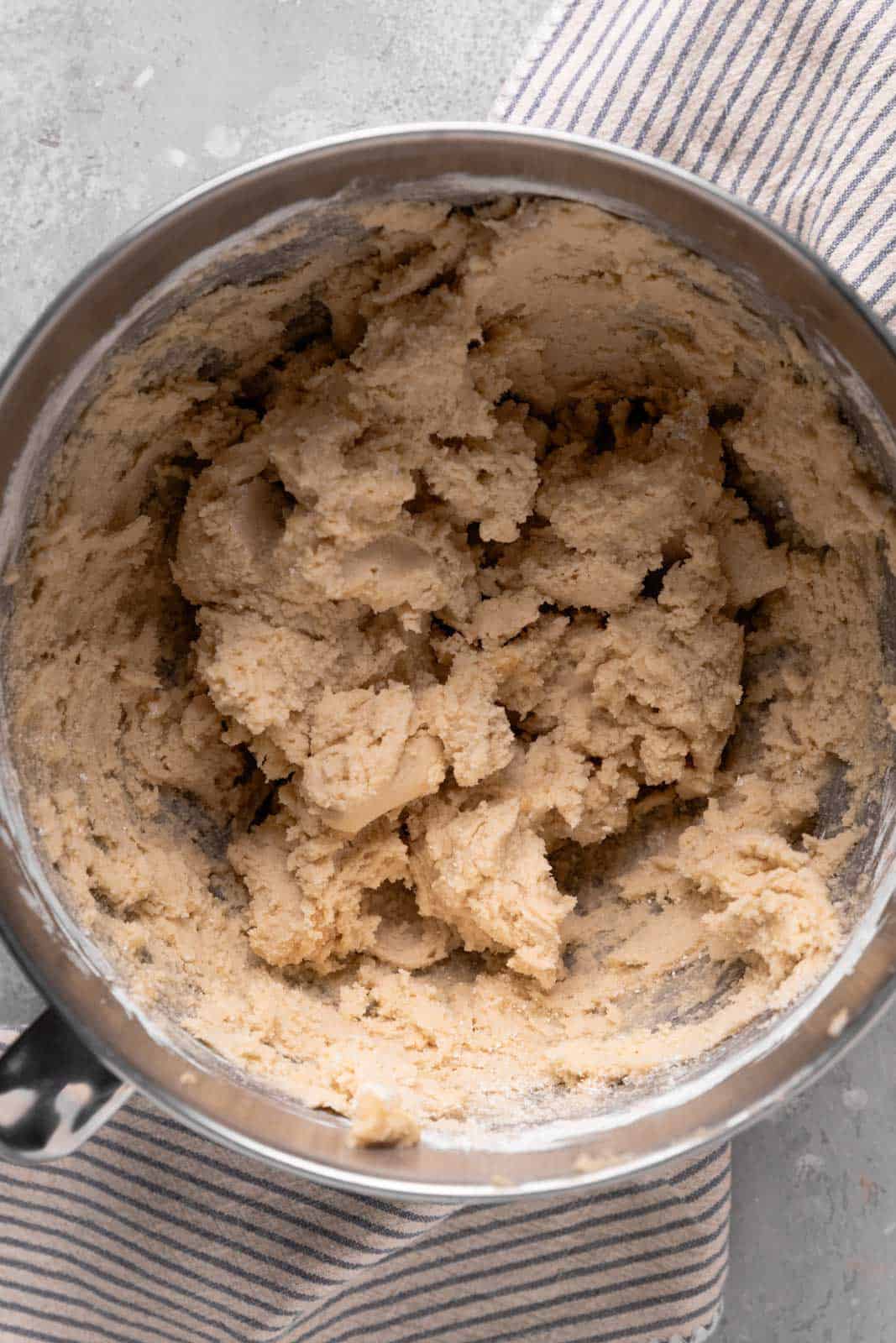 Creamed butter and brown sugar, and powdered sugar in a stand mixer metal bowl set on a flat surface with a striped linen.