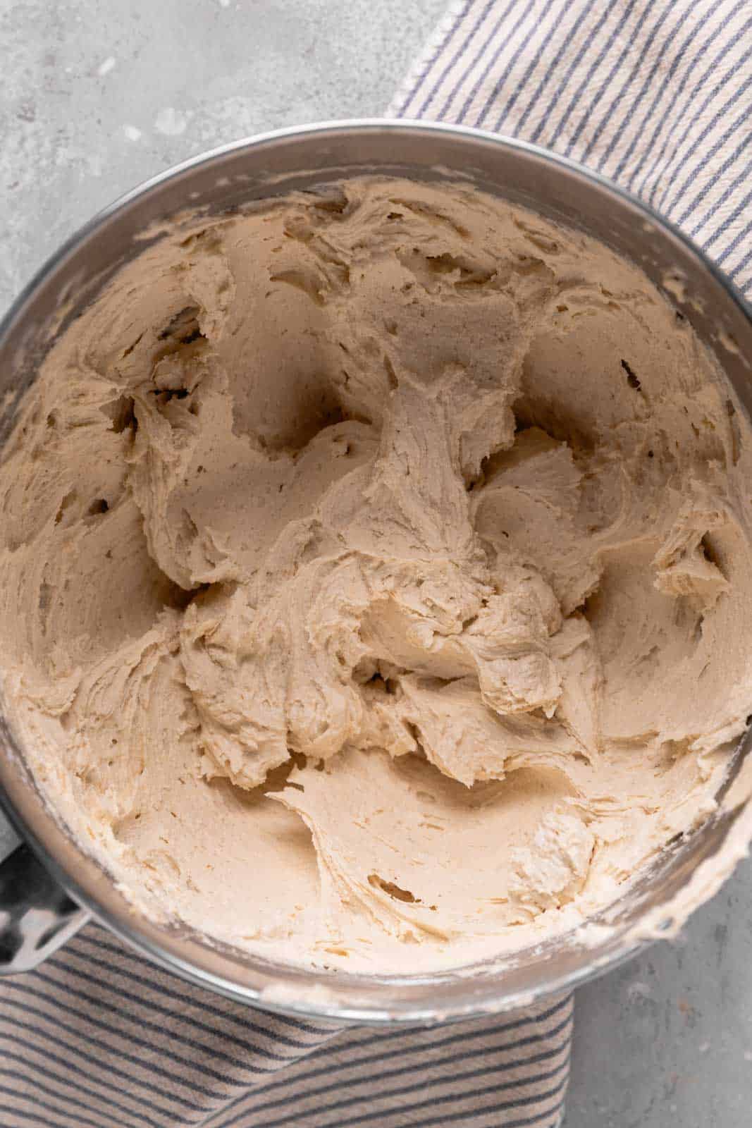 Whipped cookie dough buttercream in a stand mixer metal bowl set on a flat surface.