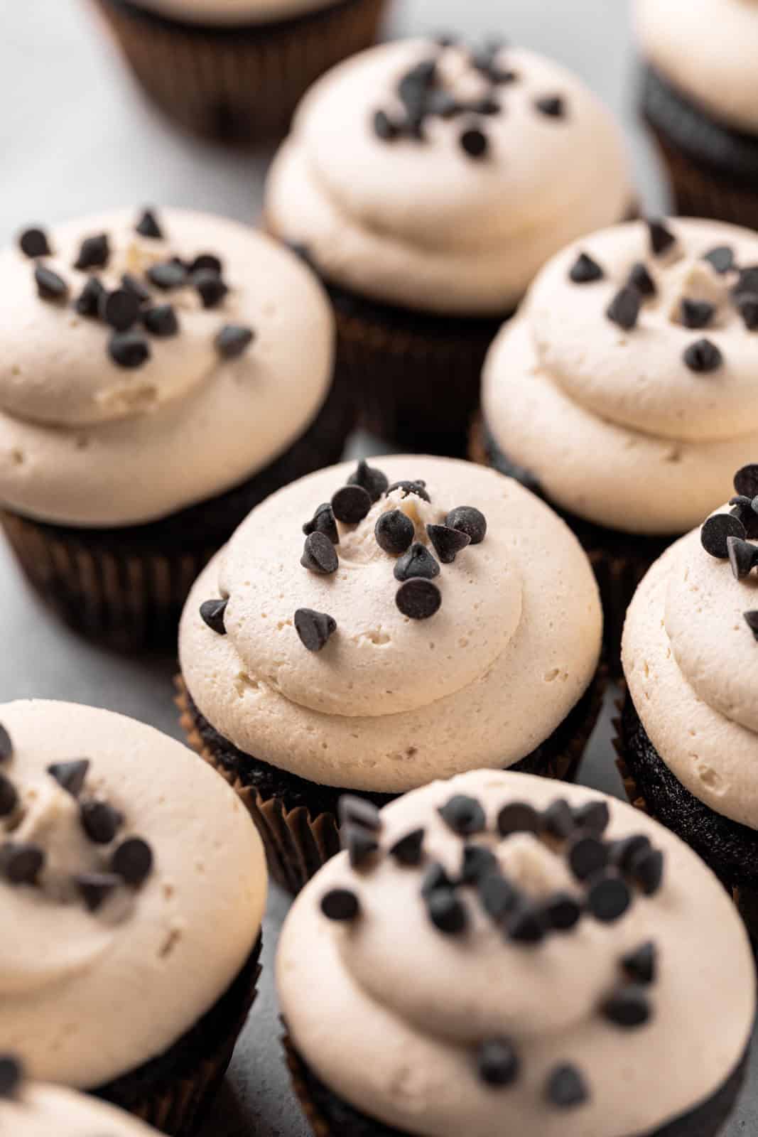 Close up angle of chocolate cupcakes topped with cookie dough buttercream and mini chocolate chip cookies.