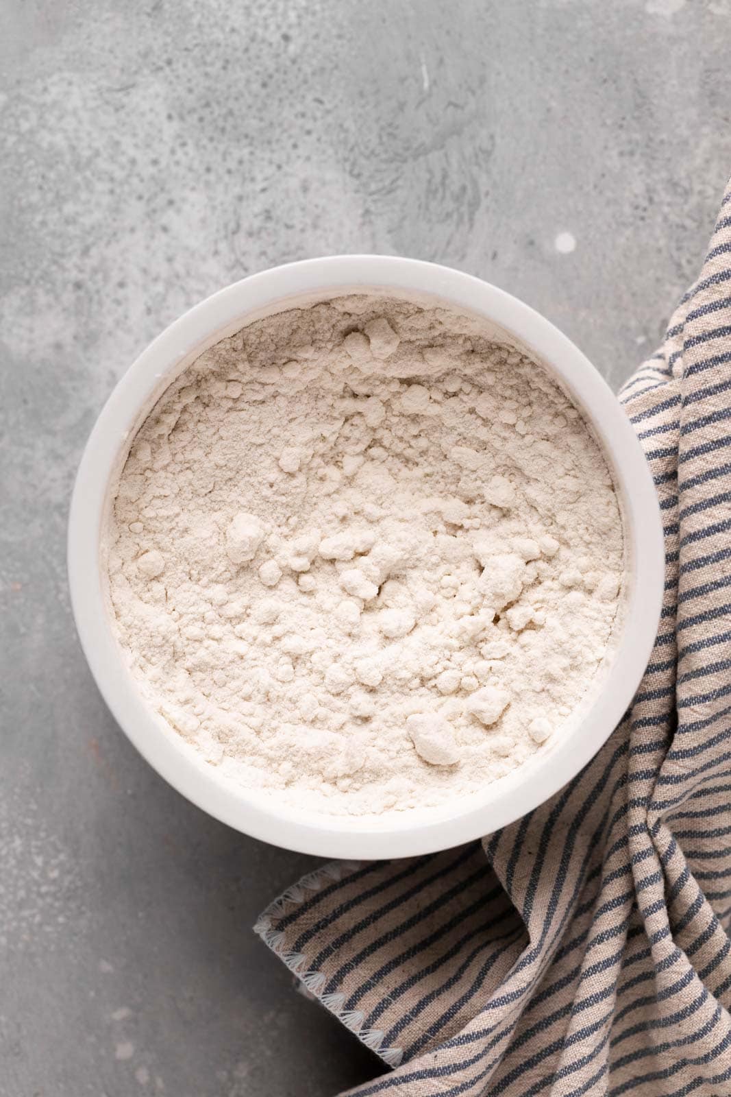 Heat treated flour in a white ceramic bowl set on a flat grey surface.