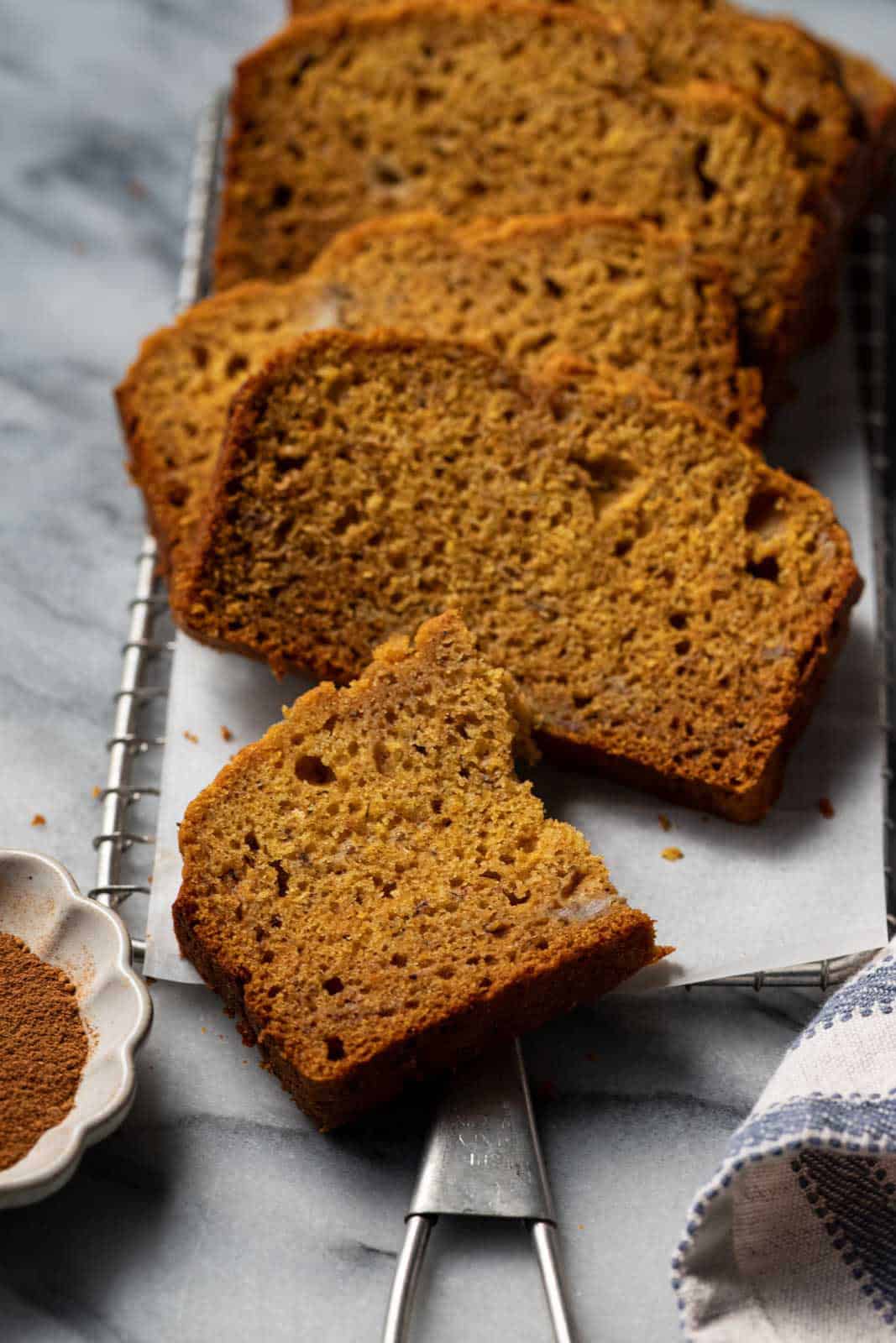 Sliced banana pumpkin bread layered on parchment on a marble surface.