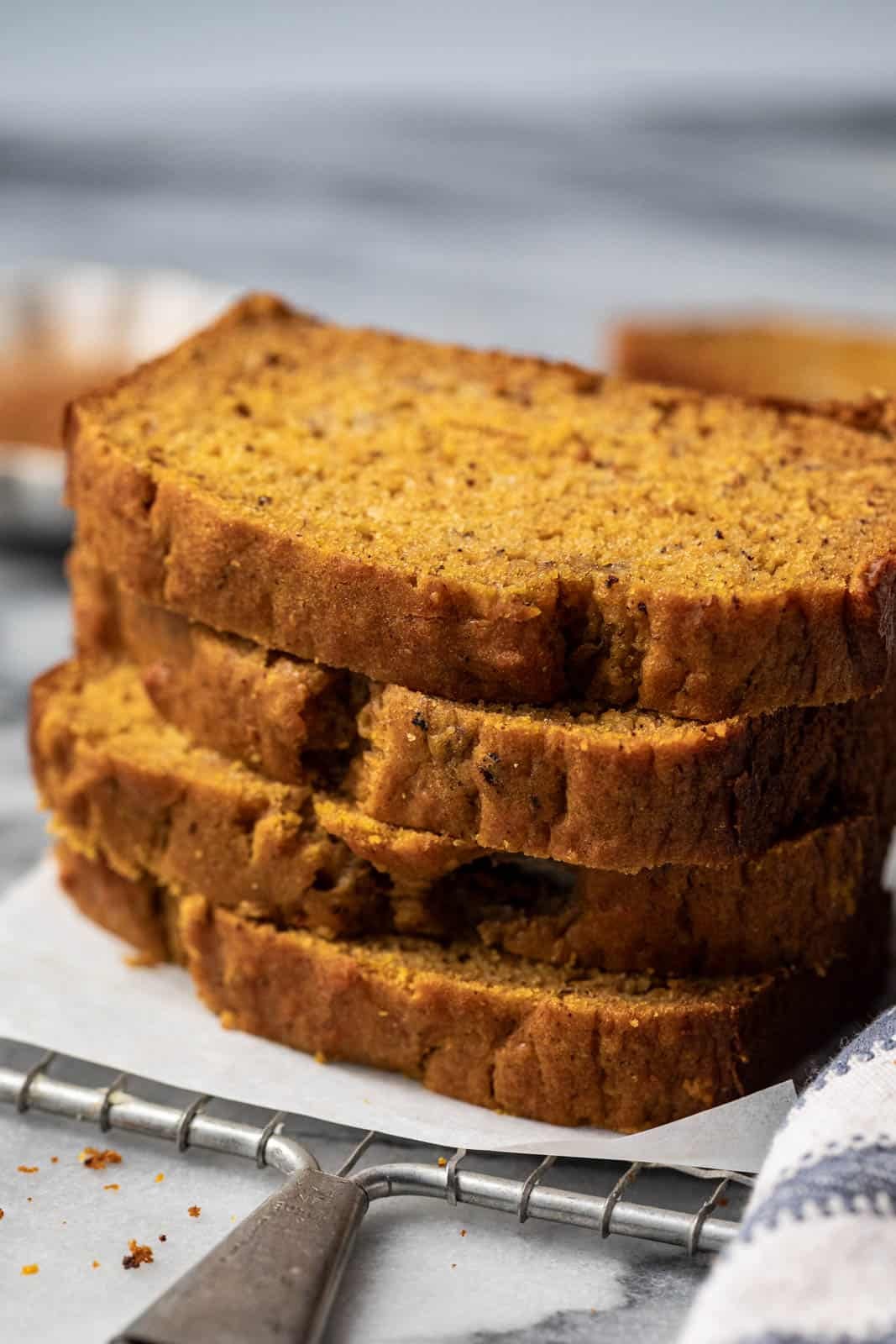 Close up of stacked slices of pumpkin banana bread on a rectangular wire rack with parchment.
