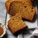Sliced banana pumpkin bread layered on parchment on a marble surface.