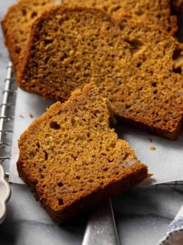 Sliced banana pumpkin bread layered on parchment on a marble surface.